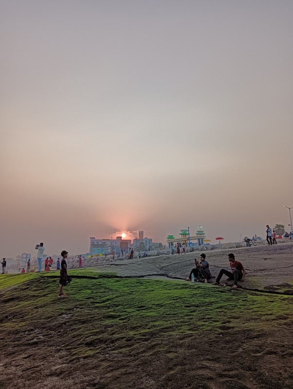 A cool-toned image of a sunset on a beach. Several beach-goers sit on the sand. 