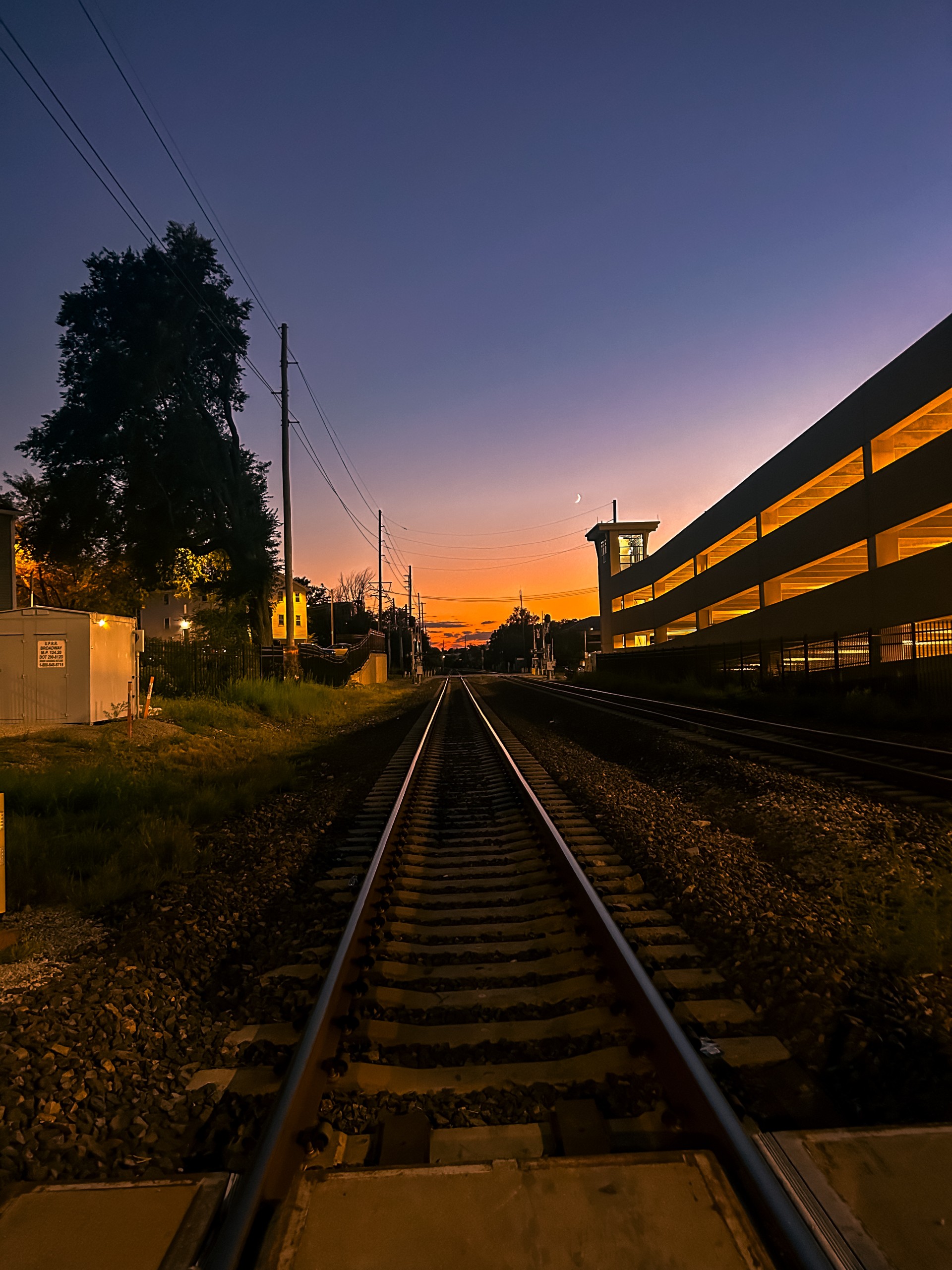 Train tracks run through the center of the image, with a beautiful orange and purple sunset sky. 